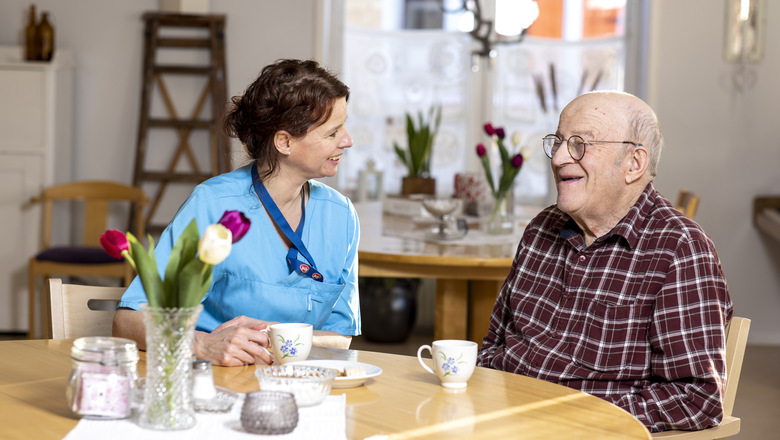 En kvinna och en äldre man samtalar över en kopp kaffe.