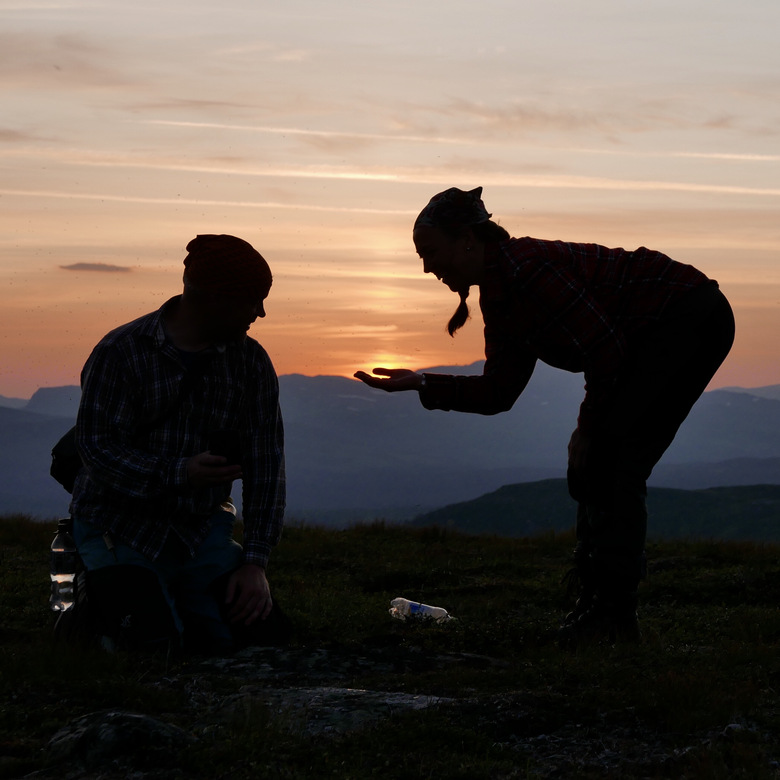 Två personer på ett fjäll där en håller solnedgången i sin hand