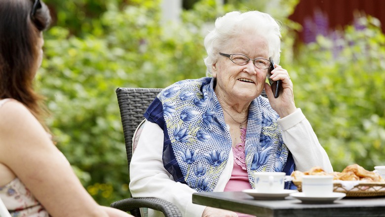 äldre kvinna talar i telefon vid fikabordet i trädgården