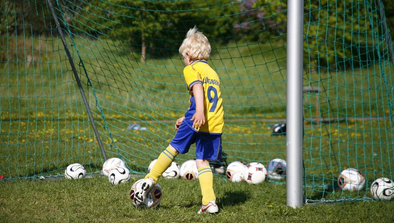Lite pojke i svensk landslagsdräkt spelar fotboll.