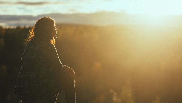 Bild på kvinna som sitter på en stubbe och tittar på solnedgången