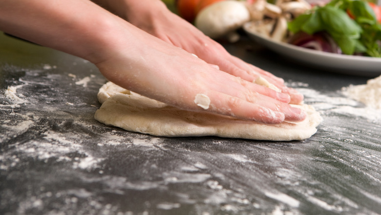 A pair of female hands prepare some bread dough on the counter for pizza.