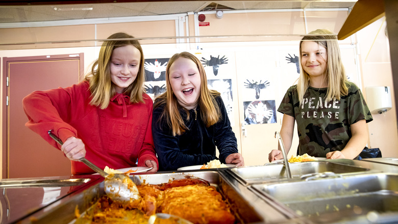 Tre glada flickor tar mat från en skolbespisning.
