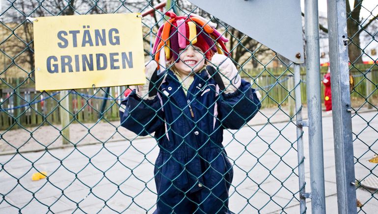 Ett barn bakom en grind med en skylt som säger "Stäng grinden"